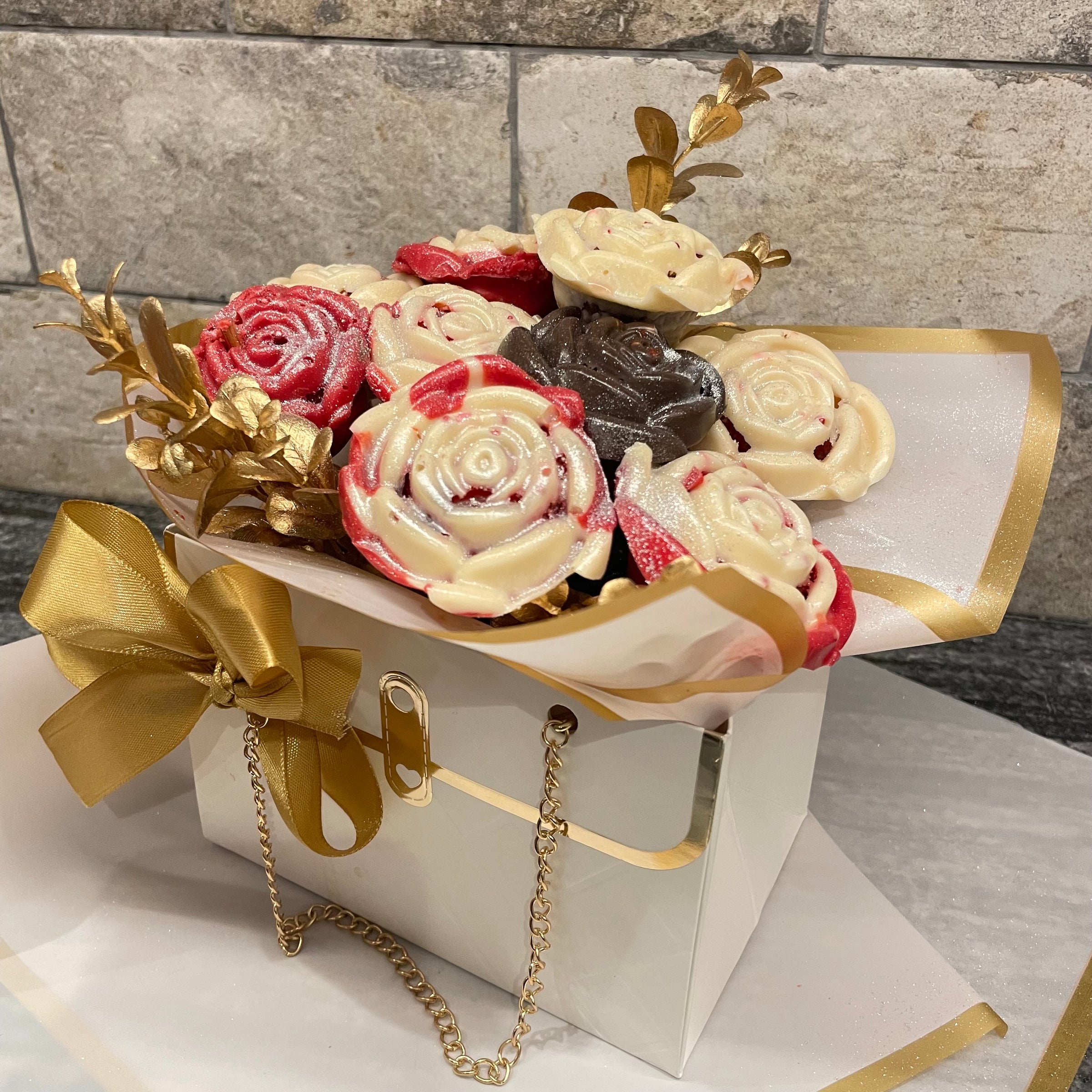 Bouquet of cookies shaped like flowers in a decorative box with gold accents on a stone surface.
