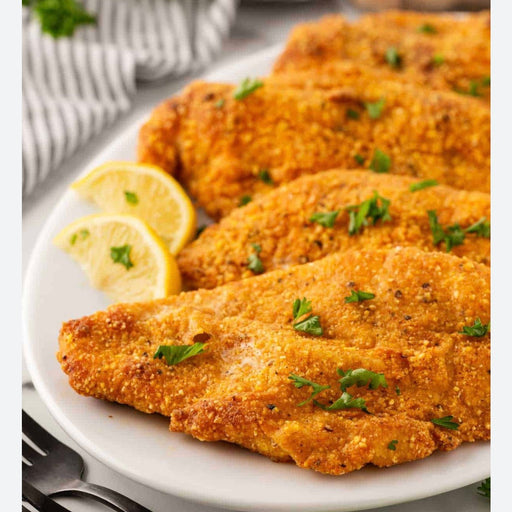Breaded chicken cutlets on a plate with lemon wedges and parsley.