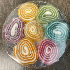 Colorful swirled gummy candies on a clear plate with a wooden surface background.