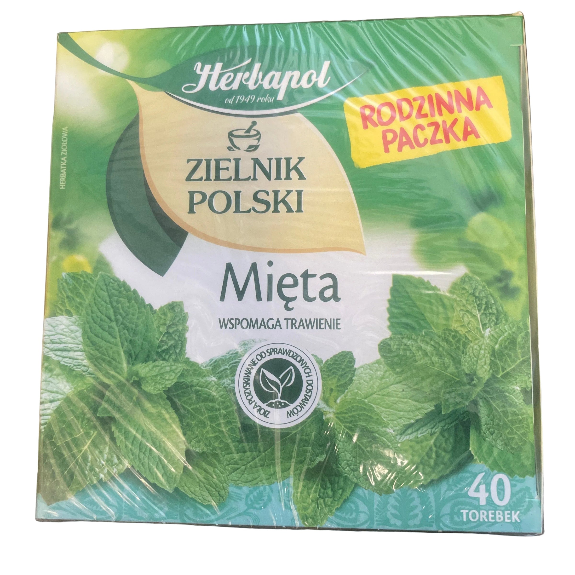 A box of Polish herbal tea, 'Zielnik Polski Mięta' (Mint), placed on a dark wooden table. The packaging features green mint leaves, a yellow leaf logo, and a yellow 'Rodzinna Paczka' (Family Pack) sticker.