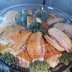 Platter of assorted sandwiches with deli meats and cheeses on a clear plastic tray.