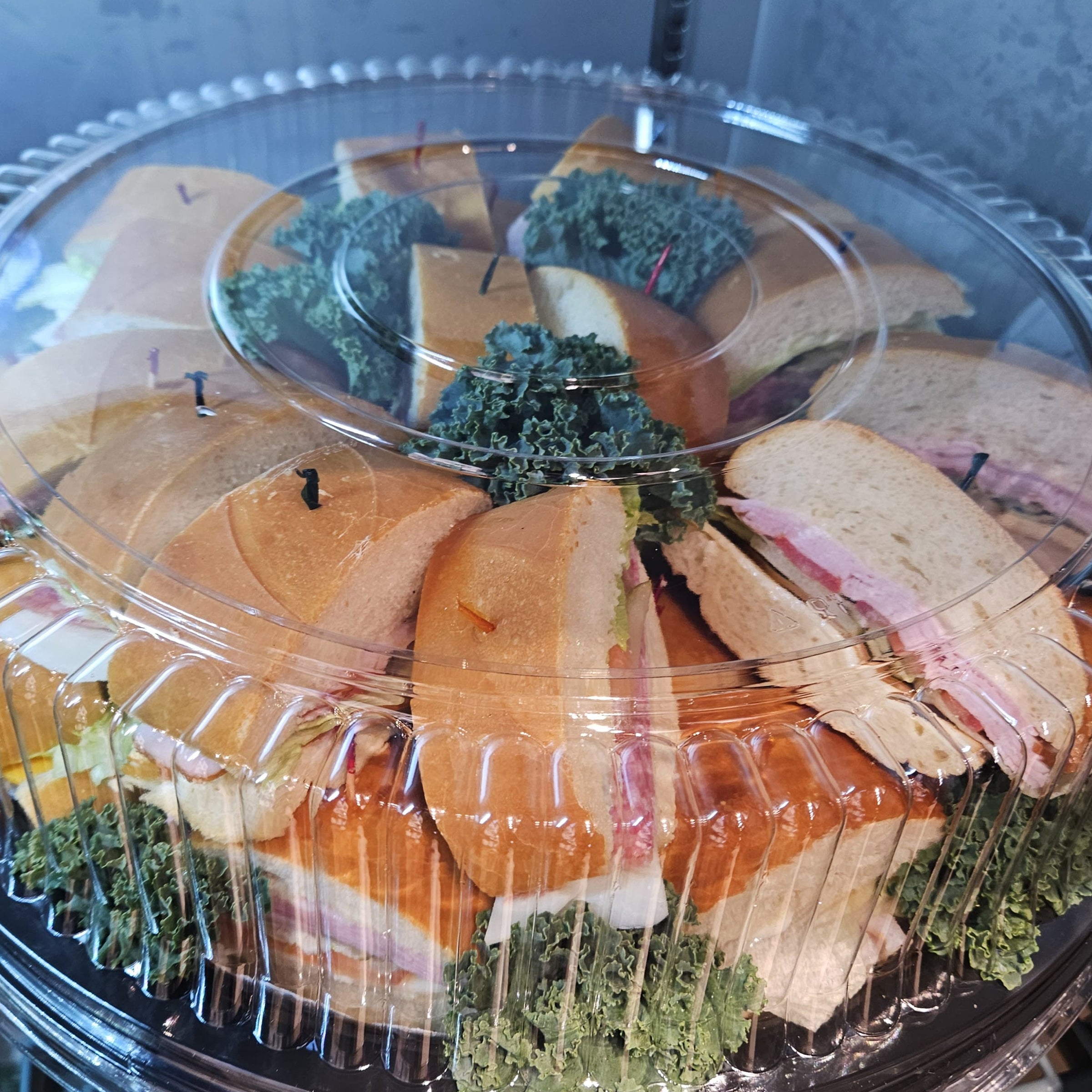 Platter of assorted sandwiches with deli meats and cheeses on a clear plastic tray.