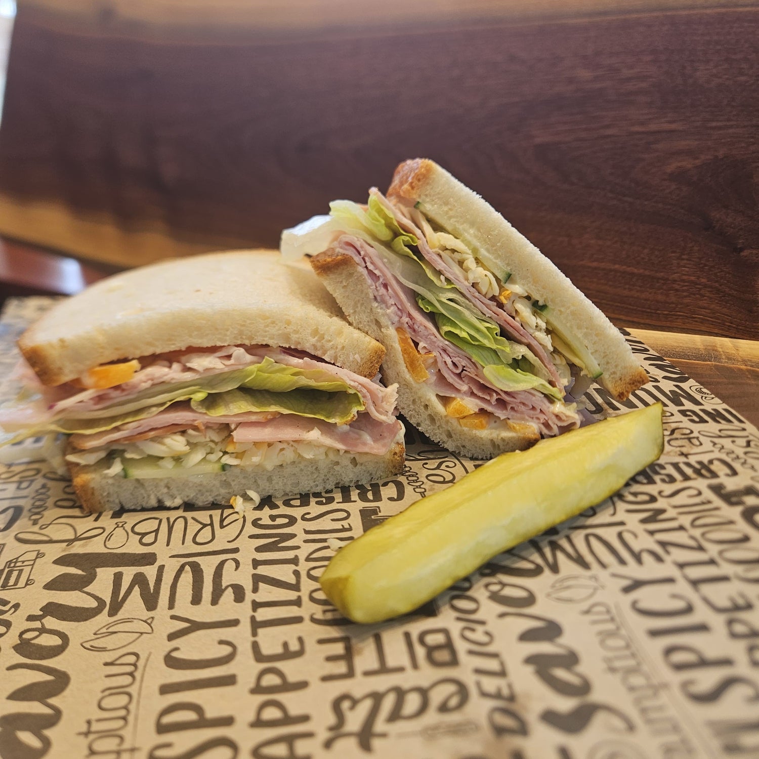 Half-cut sandwich with a pickle on a paper with text, on a wooden surface