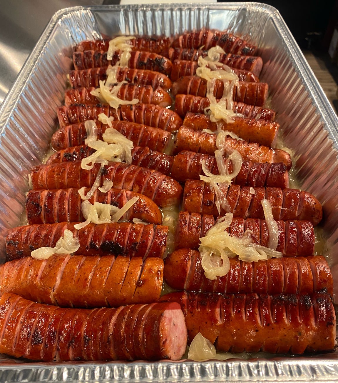 Stacked hot dogs with onions in a metal tray